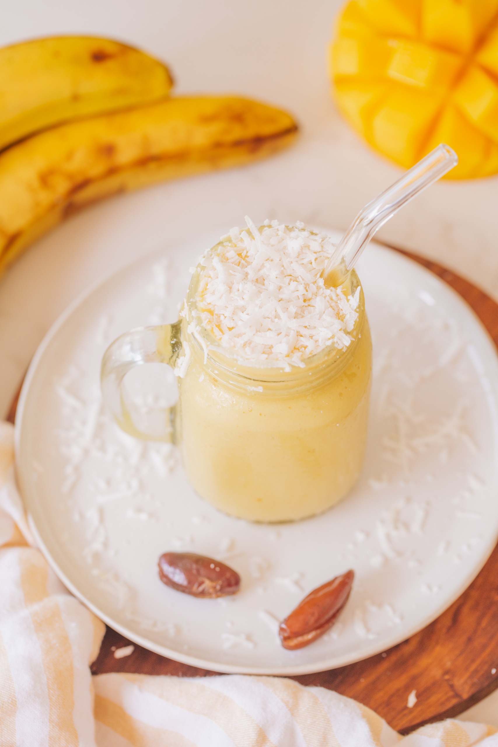 mango and banana sunshine smoothie with coconut on top of white plate with dates
