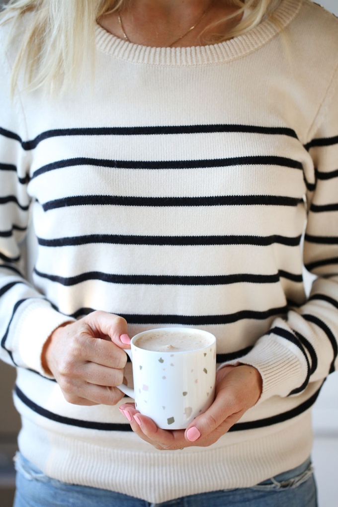 Woman in a stripey jumper holding a caramel latte in a spotty pastel mug