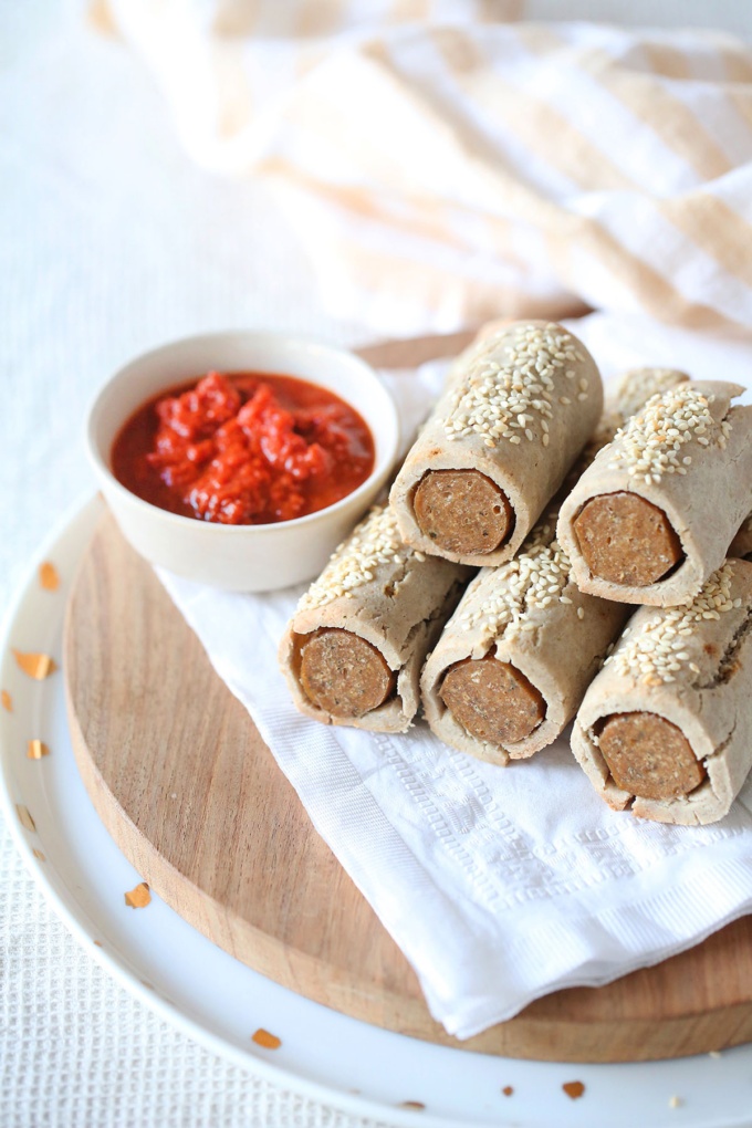 Healthy vegan sausage rolls served with a tomato dip on a wooden board with sesame seeds