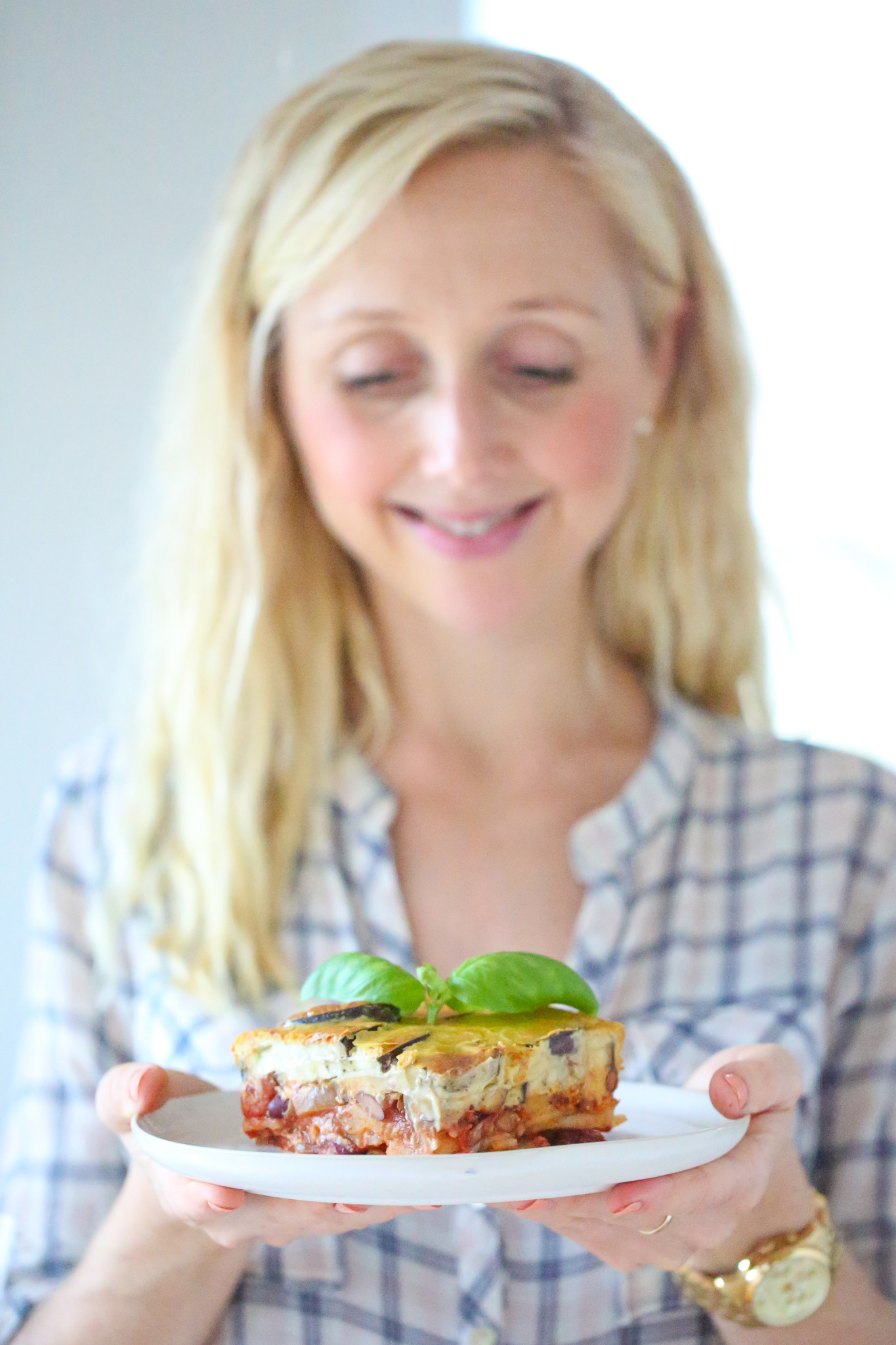 Buffy Ellen holding Glorious Greek Moussaka on white plate with basil leaf