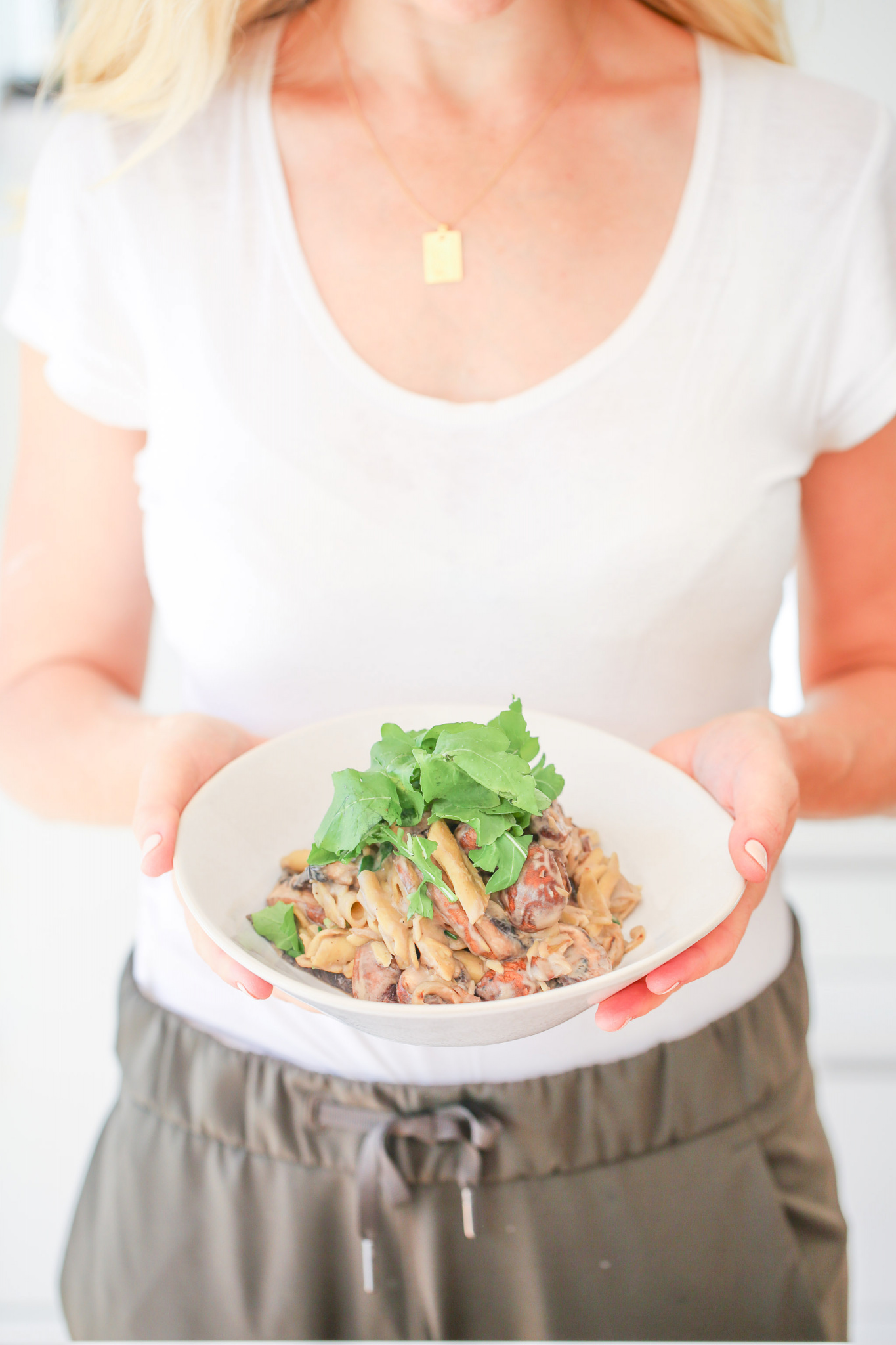 Buffy Ellen Gill holding a white bowl filled with Creamy Mushroom Penne Pasta with a handful of Rocket on top.