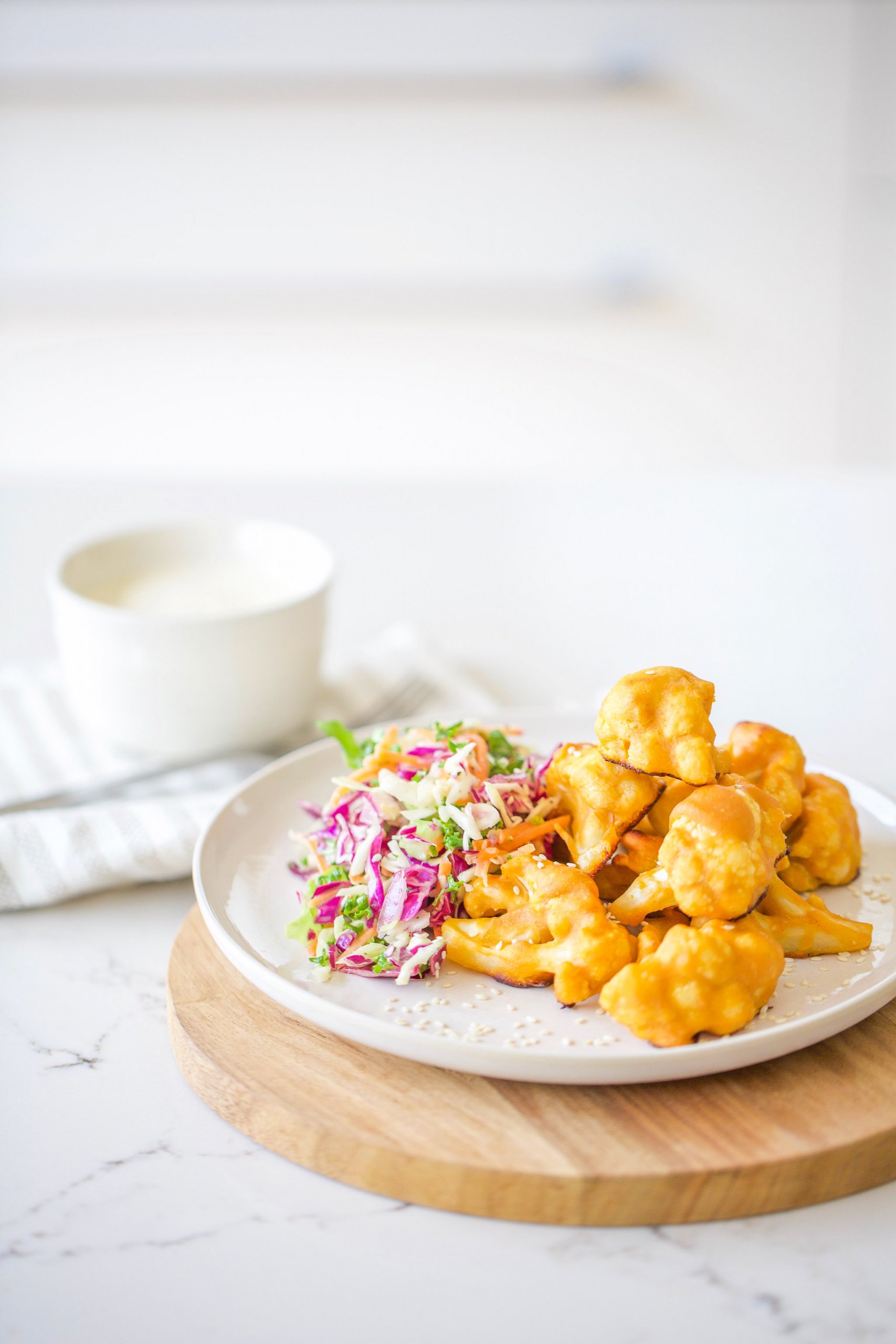 side of fried cauliflower wings on white plate with side of slaw and sliver fork