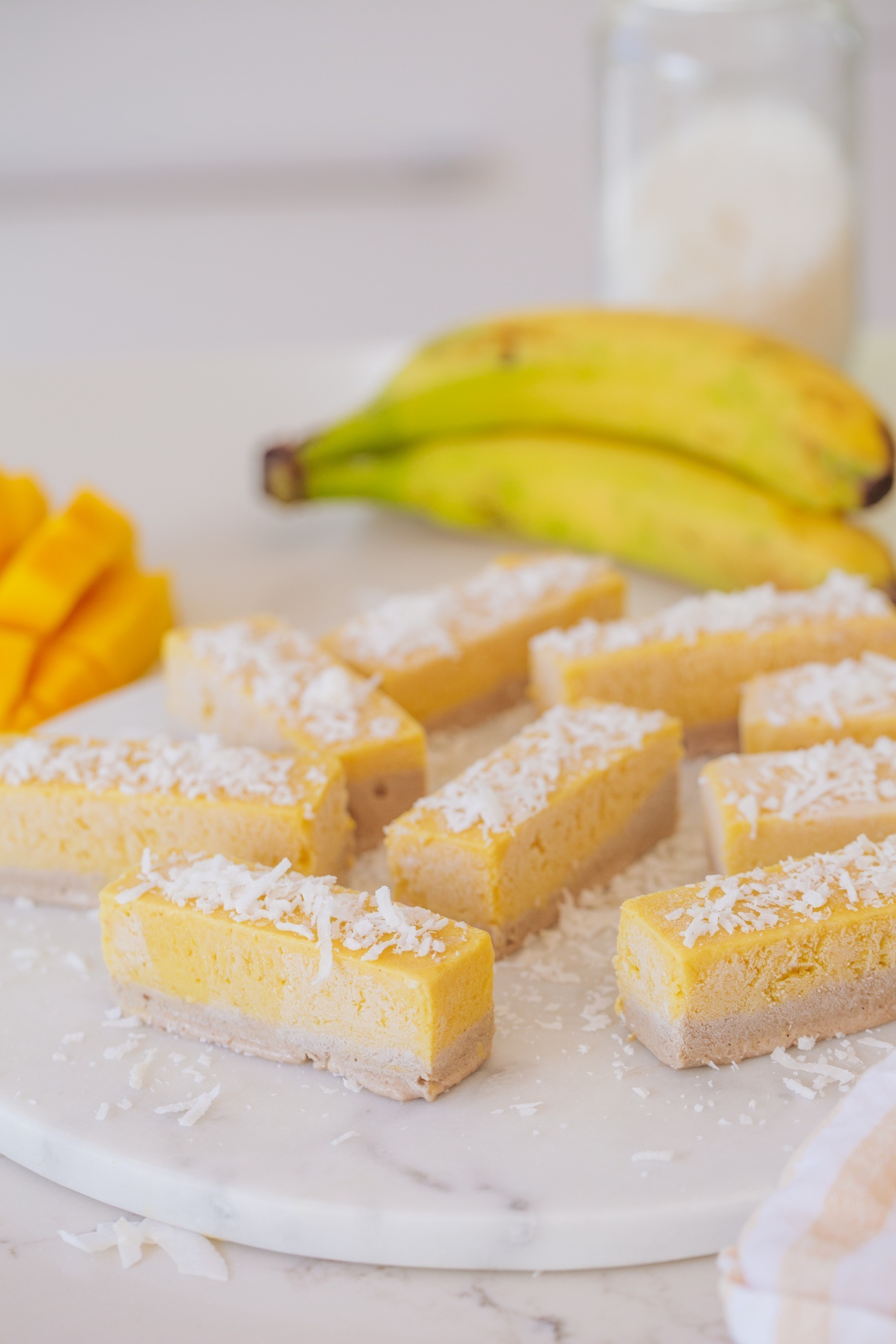 Mango banana and coconut tropical ice cream bars with shredded coconut on top and a bunch of bananas.