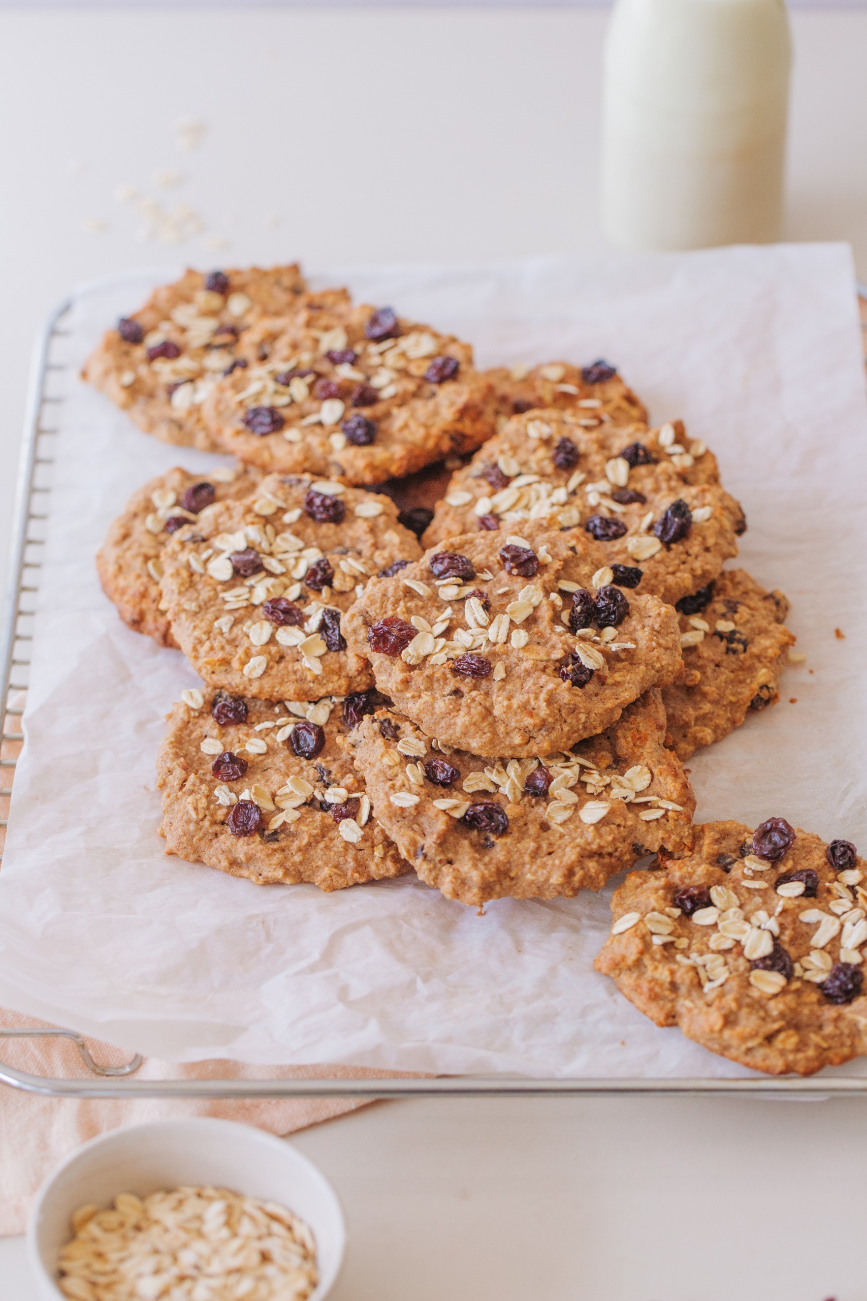 Oat and Raisin Cookies on baking tray with white paper and bowl of oats