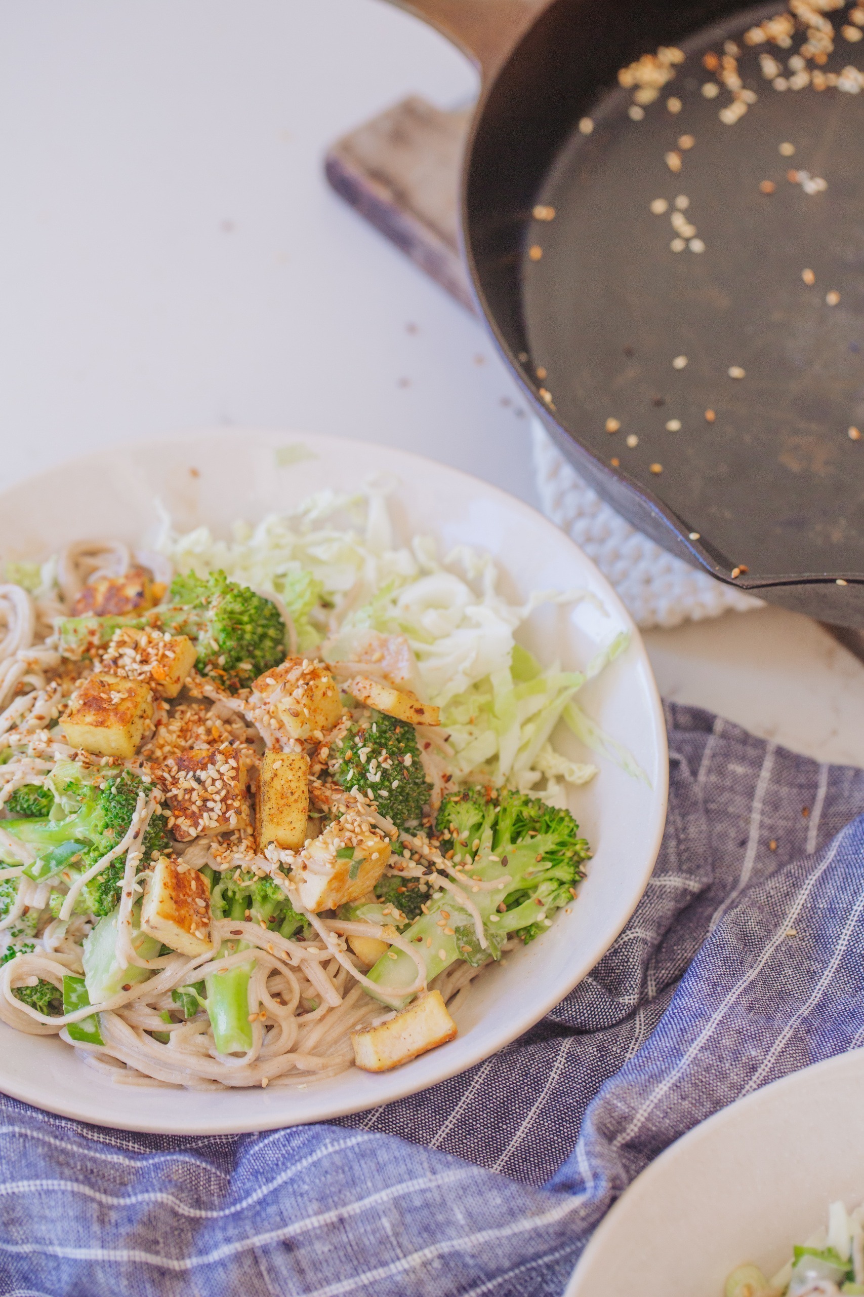 Bowl of sesame ginger noodles with broccoli tofu and sesame seeds.