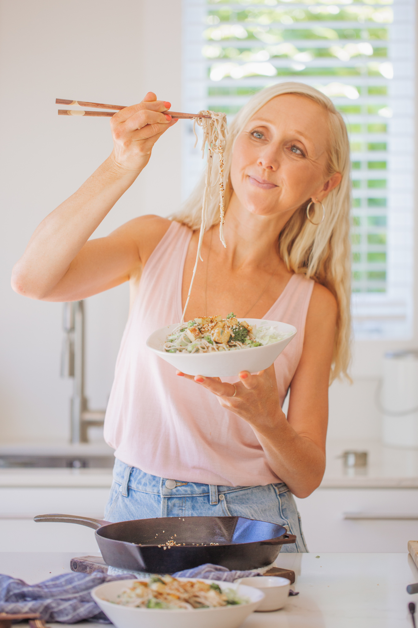 Buffy Ellen holding soba noodle from ginger sesame broccoli noodle bowl wearing pink top
