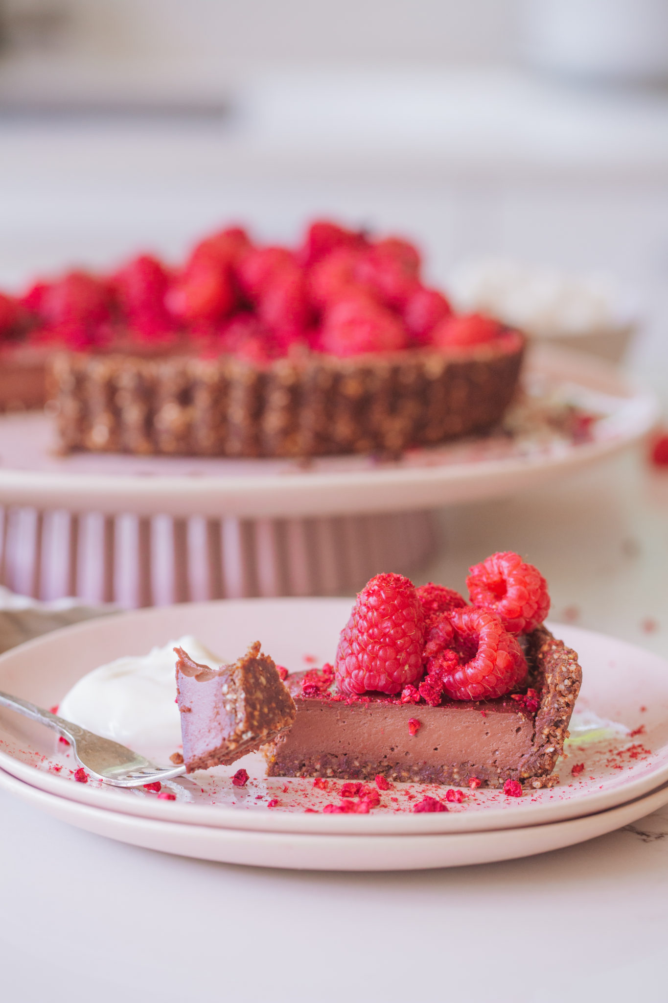 Sliced Chocolate Raspberry Tart, covered in raspberries, cacao nibs on large pink plate with fork 