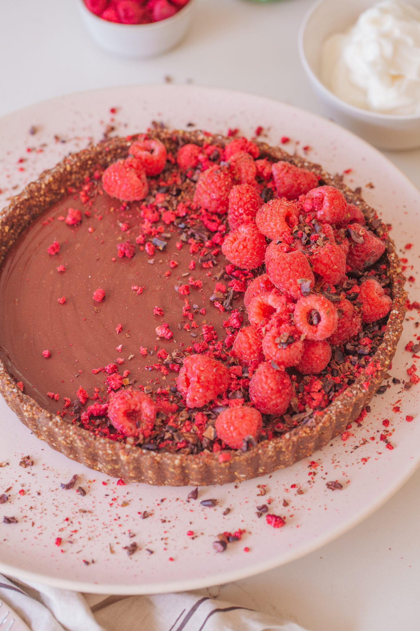 Top down of Chocolate Raspberry Tart, covered in raspberries, cacao nibs on large pink plate