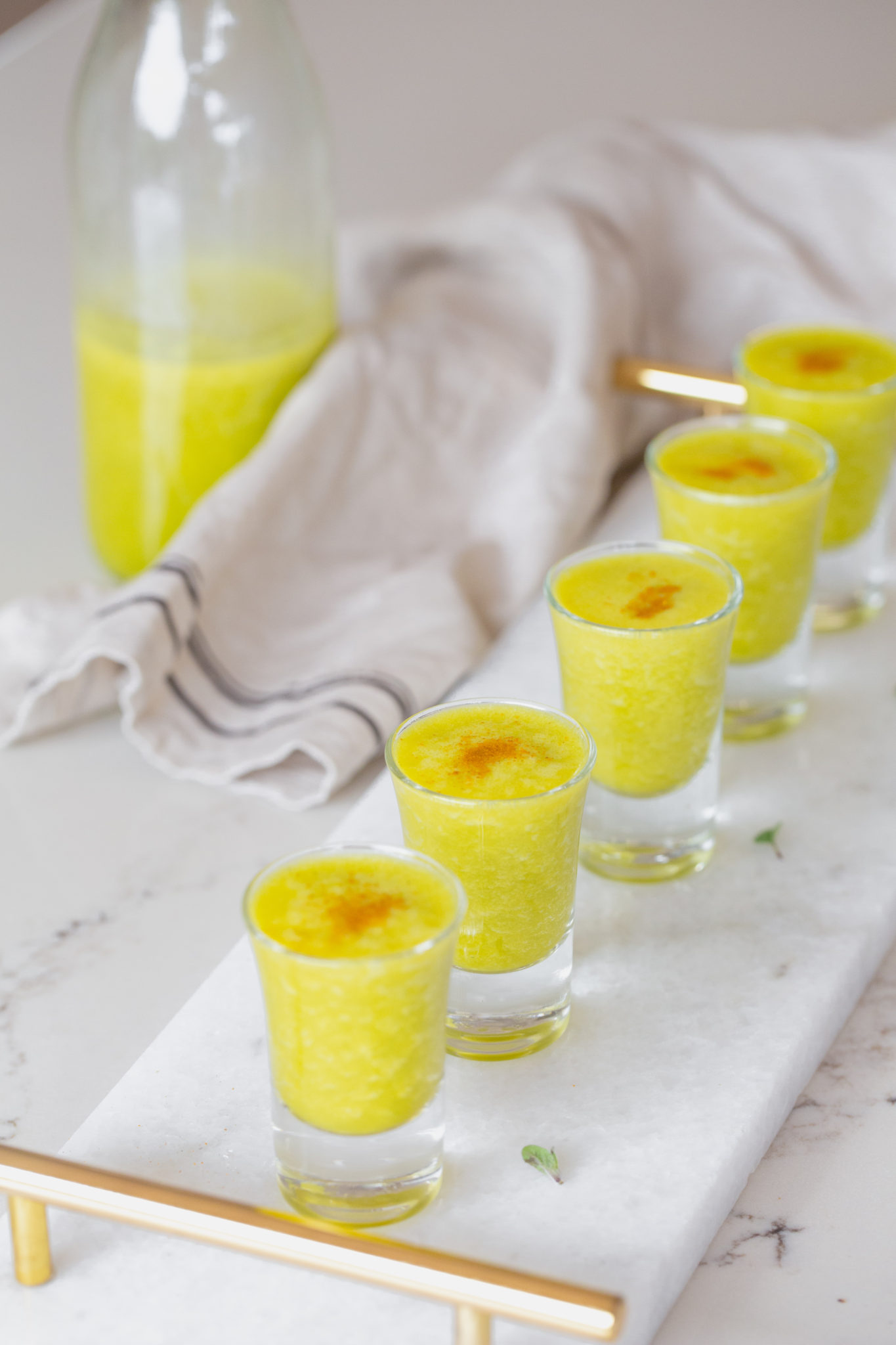 Line up of Flu Shot Juice with turmeric sprinkled on a white platter with cream tea towel