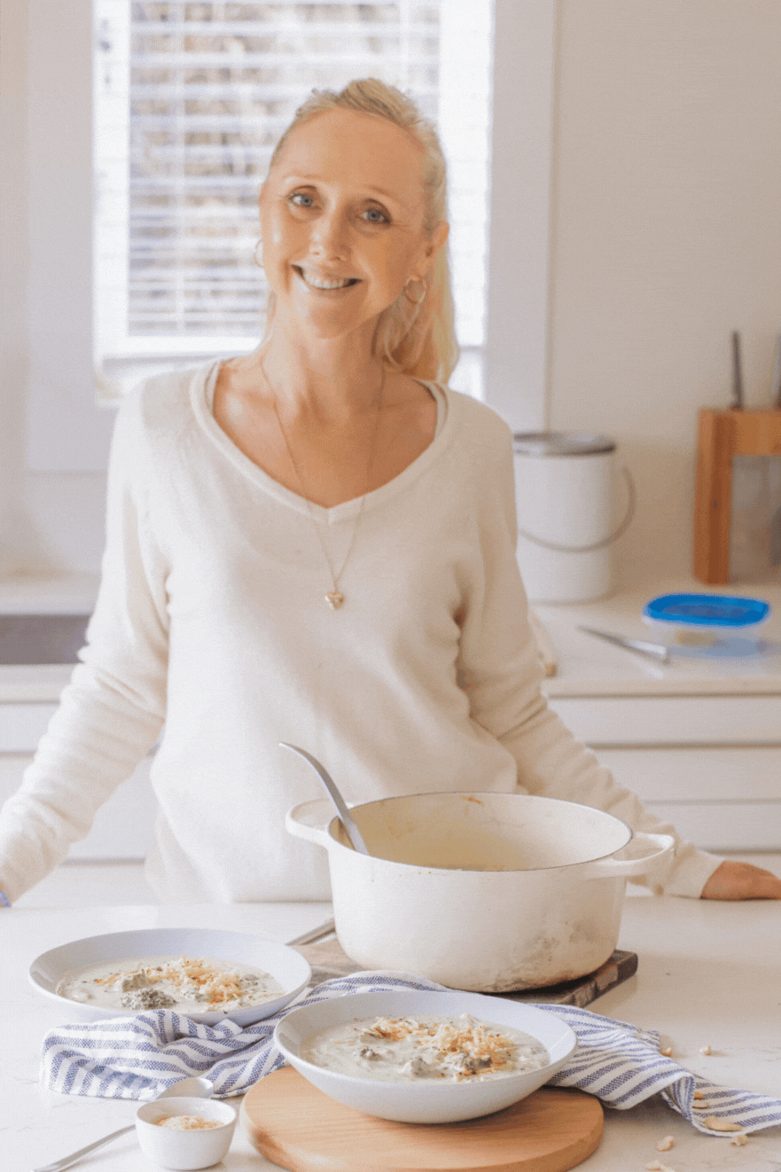 Woman (Buffy Ellen Gill) serving and smelling bowls of creamy broccoli soup topped with grated cheese.