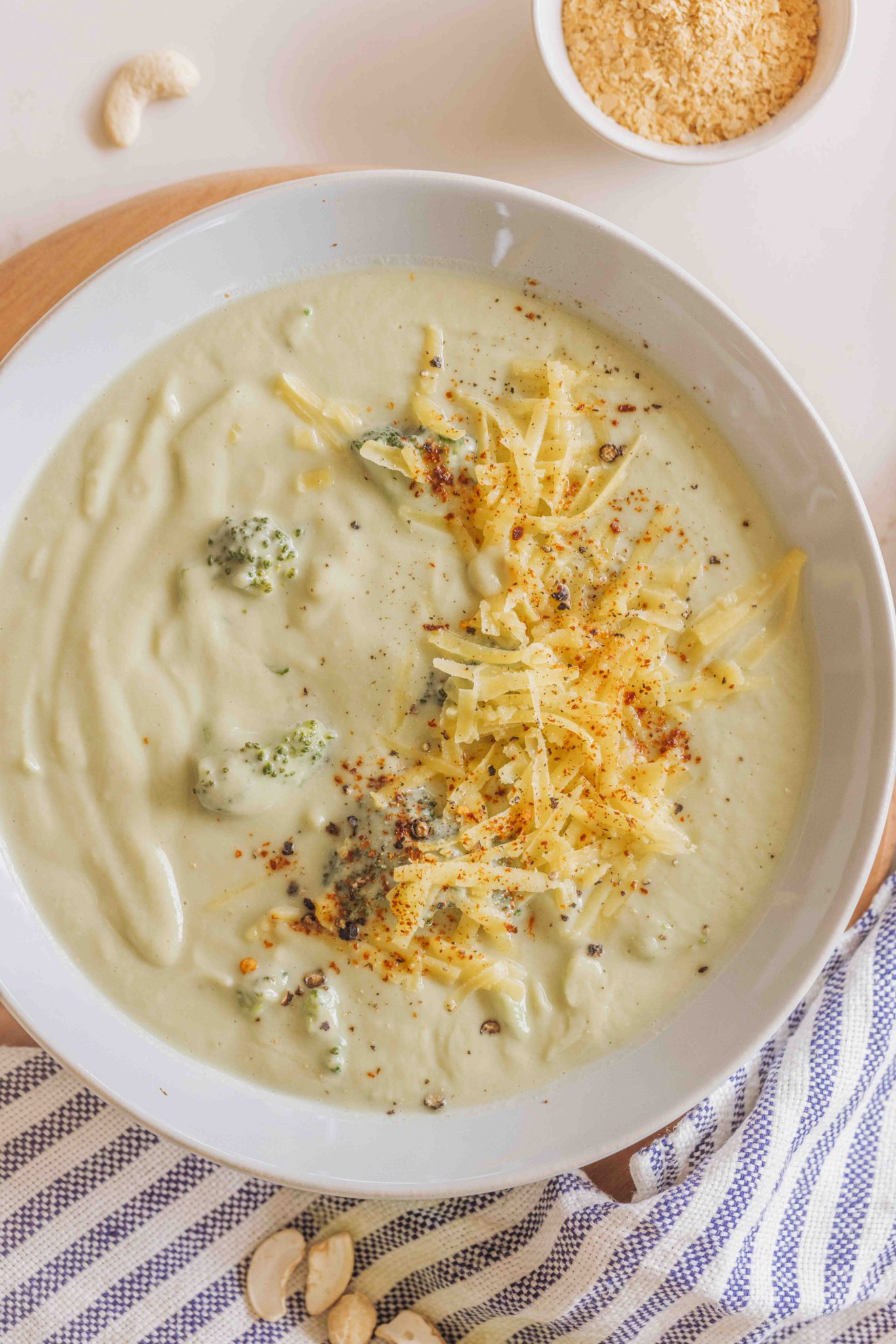 Woman (Buffy Ellen Gill) holding a bowl of creamy broccoli soup, topped with grated cheese, cracked black pepper and red chilli flakes.