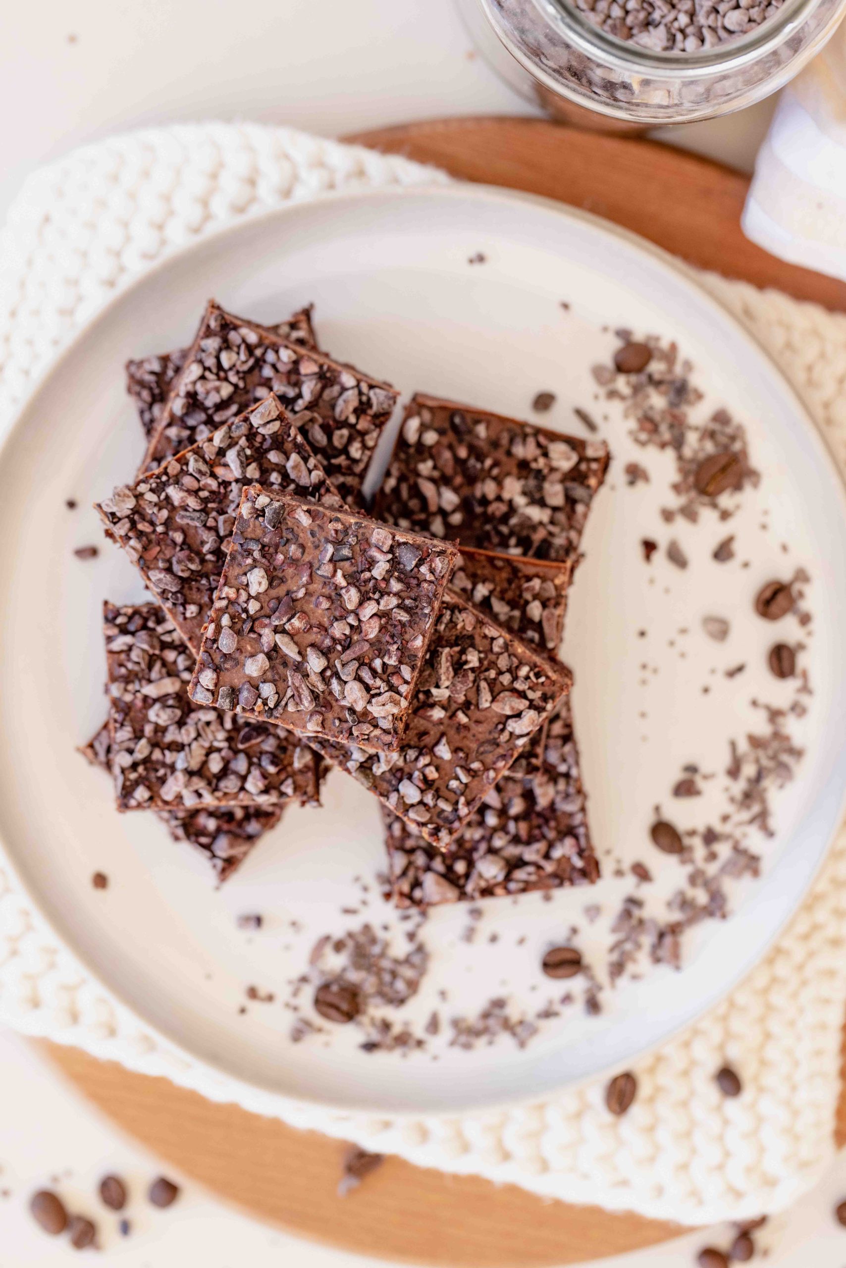 top down of raw walnut espresso brownies with almond ganache and cacao nibs on white plate