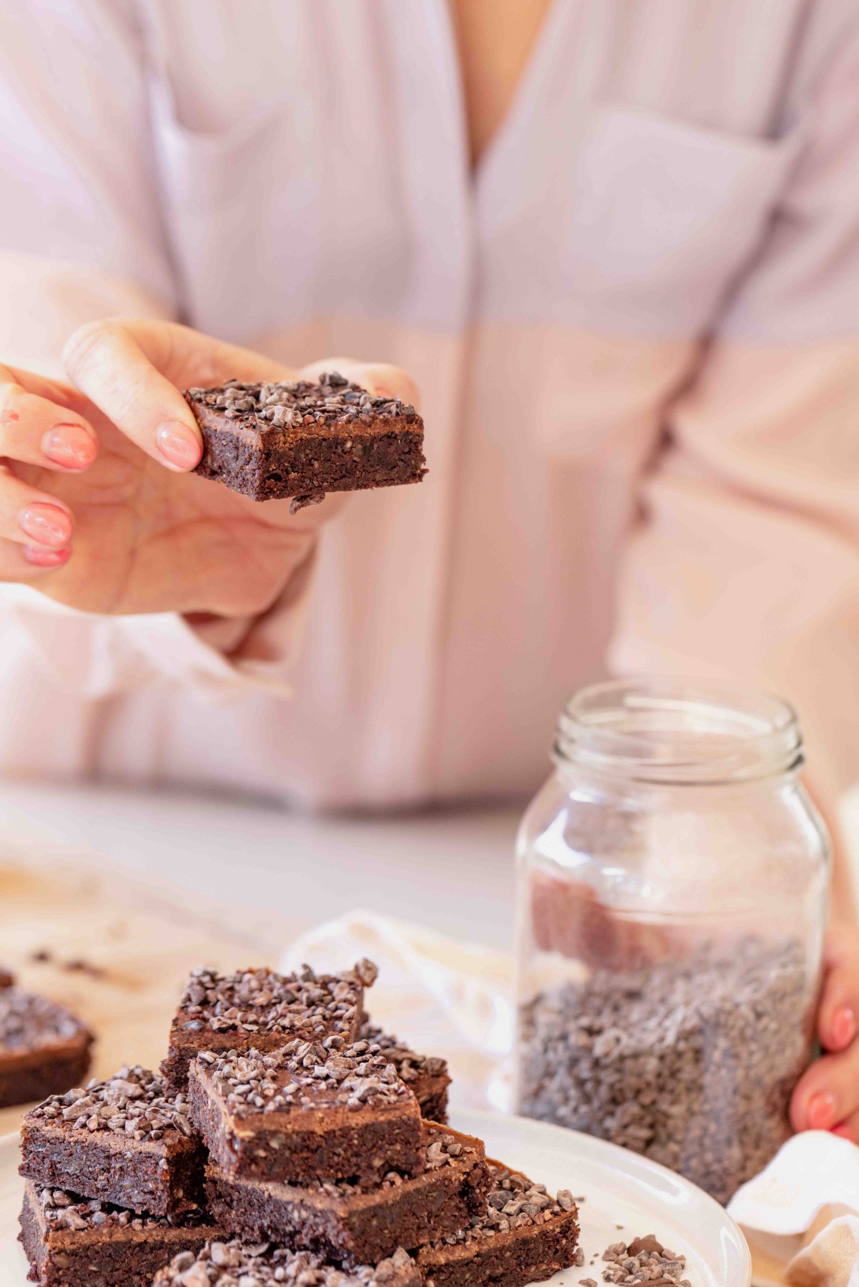 buffy ellen woman holding raw walnut espresso brownies with almond ganache and cacao nibs on white plate and jar of cacao nibs
