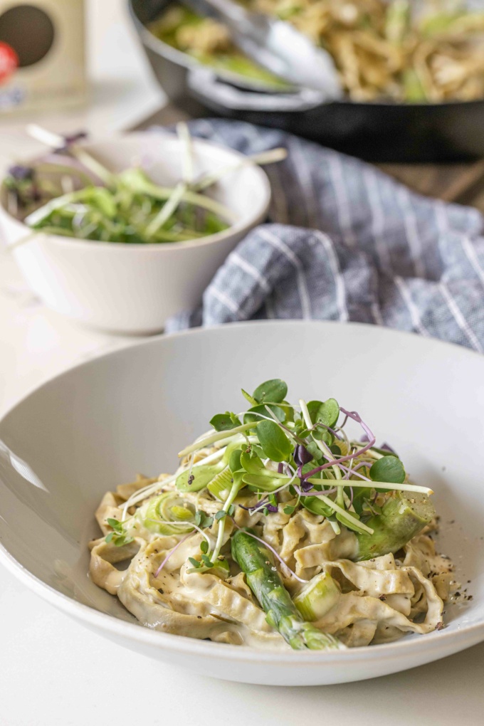 Leek and Asparagus Fettuccine Alfredo on white pasta bowl, topped with micro greens around blue table cloth