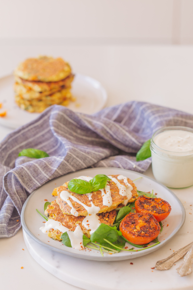 corn fritters on blue plate with charred tomato and jar of vegan aioli on blue striped cloth