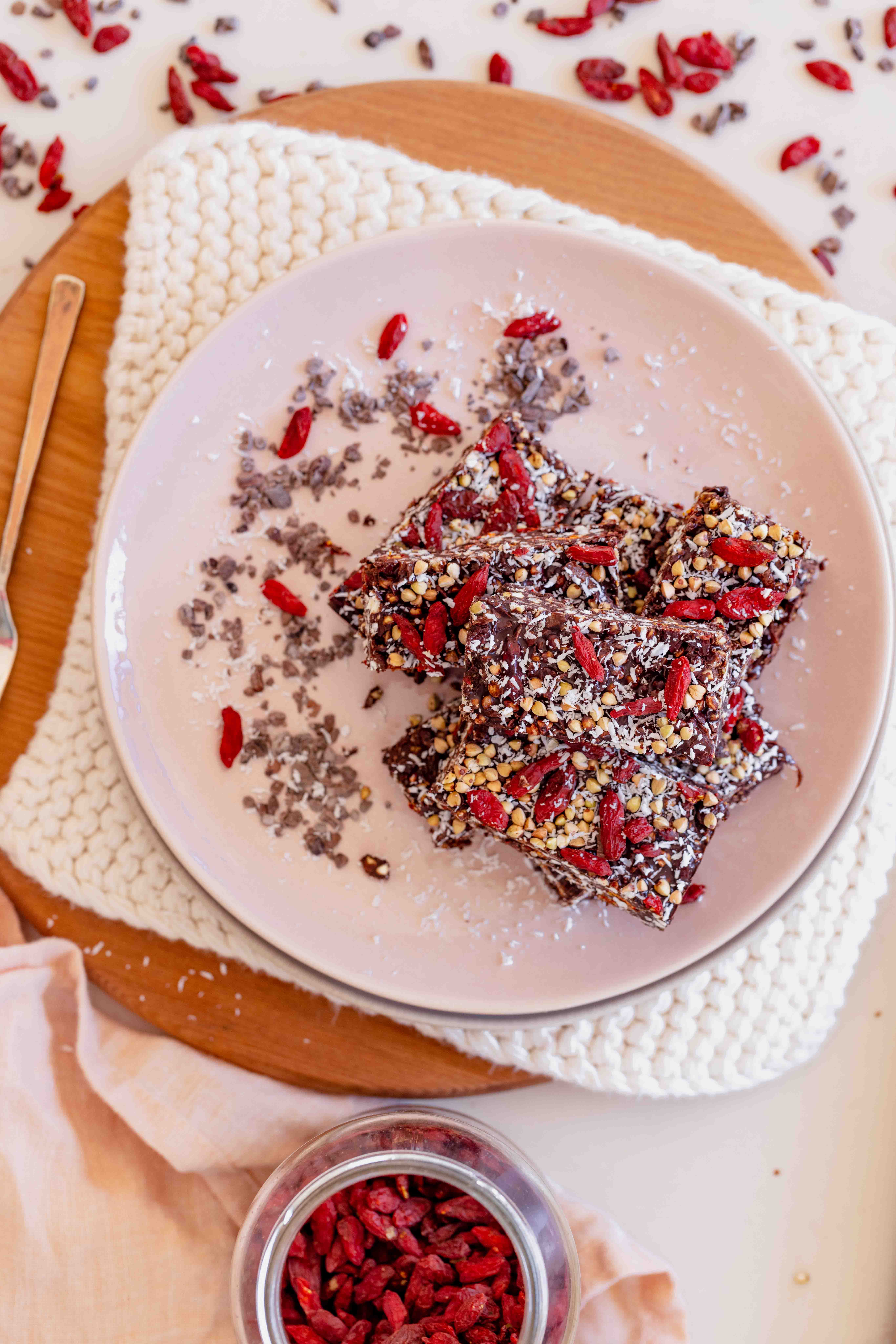 Top down of pink plate chocolate coated goji berries, buckwheat and coconut with pink nails