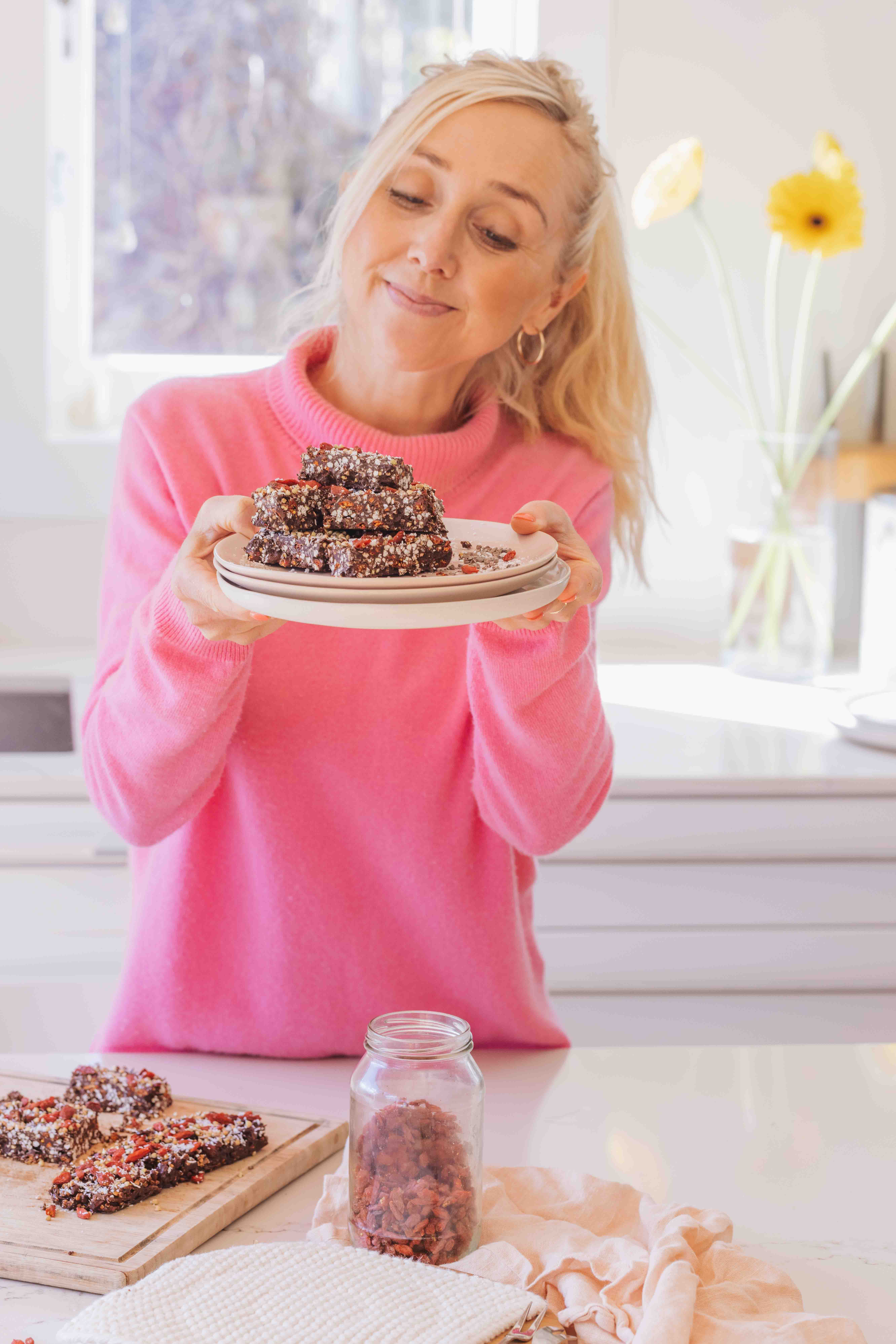 Buffy Ellen holding pink plates with chocolate coated goji berries, buckwheat and coconut crunch